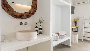 Un baño moderno con un espejo redondo, estantes blancos y un lavamanos blanco.