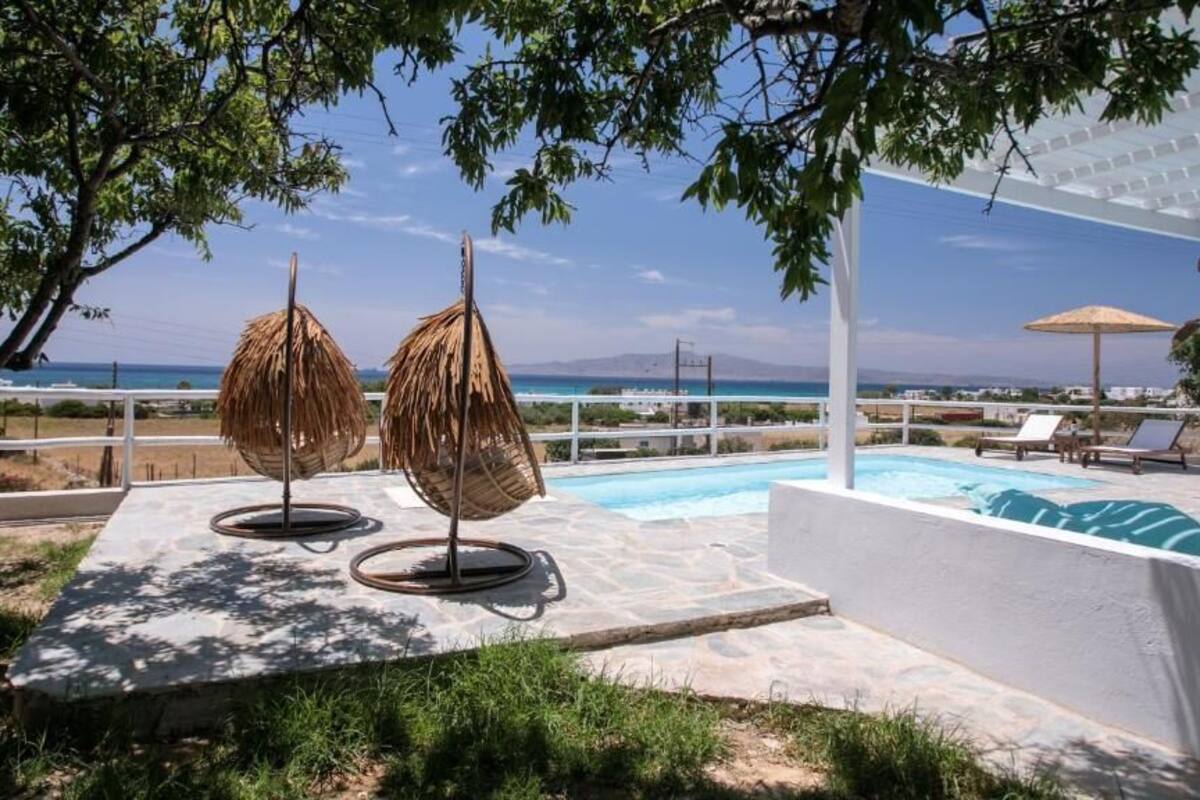 A pool area with two thatched umbrellas, a white pergola, and a view of the ocean.