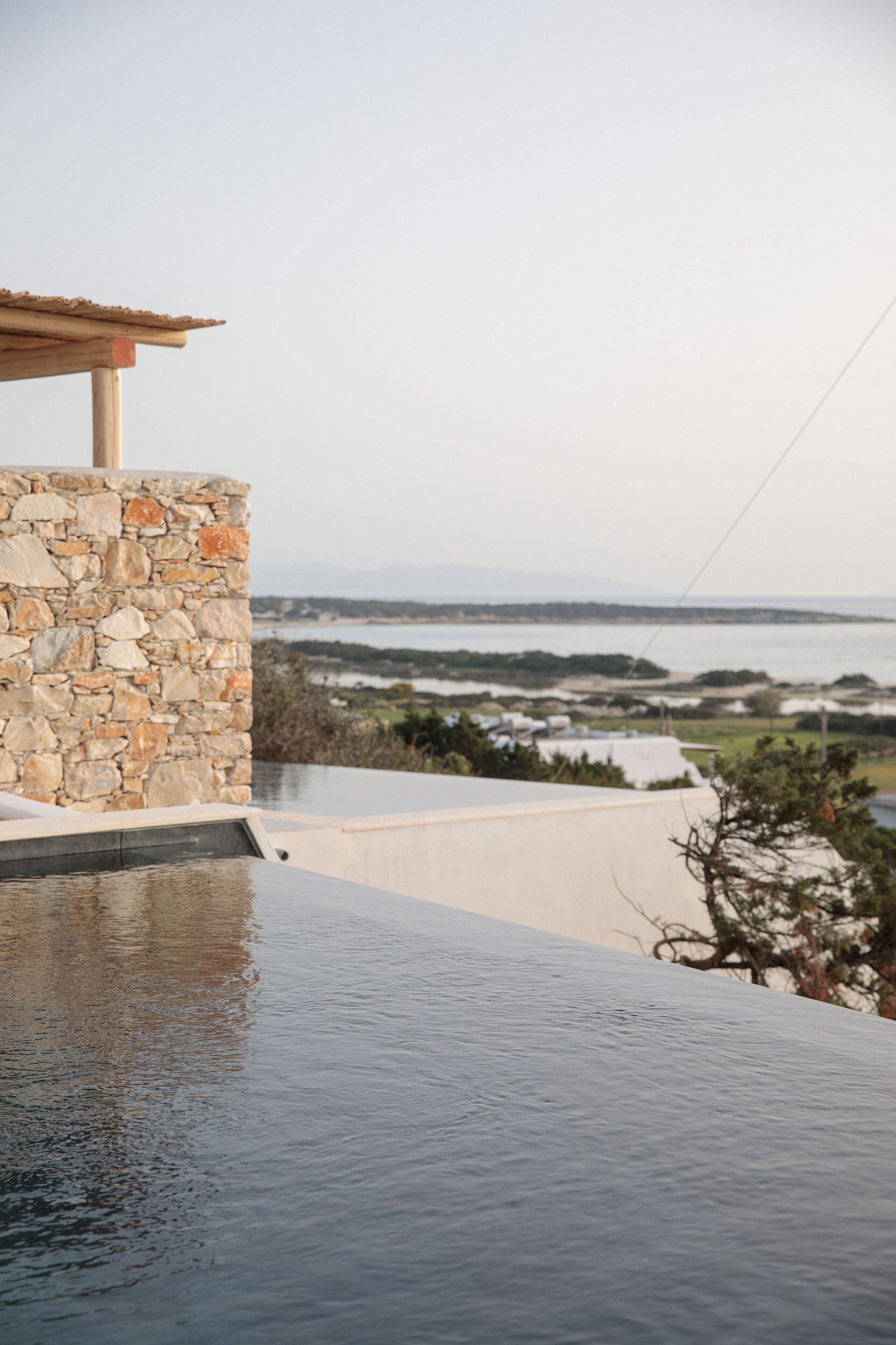 A stone wall with a wooden roof overlooking a body of water and distant landscape.