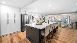 A modern kitchen with white cabinets, a stainless steel refrigerator, and a central island with chairs. - ~Villa Bella Vista~ Luxury on Lake Austin (Austin)
