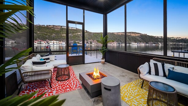 Un espace extérieur moderne, aménagé avec un foyer, un canapé et offrant une vue sur un lac et des collines.