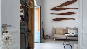 A hallway with a wooden door, a white wall with three wooden paddles, a beige sofa, and a small table with a blue object. - Queen's Hawk Case (Filicudi Porto)