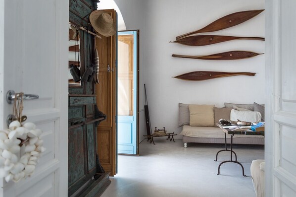 Een gang met een houten deur, een witte muur met drie houten flippers, een beige bank en een kleine tafel met een blauw object.