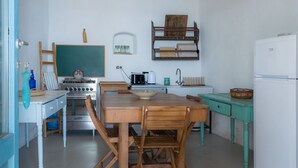 A compact kitchen with a wooden table and chairs, a stove, a sink, and a refrigerator. - Queen's Hawk Case (Filicudi Porto)