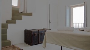 A bedroom with a bed, a window with a view, a staircase, and a suitcase. - Queen's Hawk Case (Filicudi Porto)