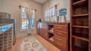 A kitchen with a refrigerator, microwave, wooden cabinets, a sink, and a window with curtains.