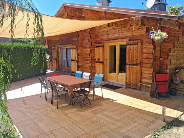 A wooden cabin with a patio, outdoor seating, and a hanging flower basket.