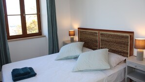 Una cama bien hecha con dos almohadas, una lámpara de noche y una toalla doblada en la mesita.