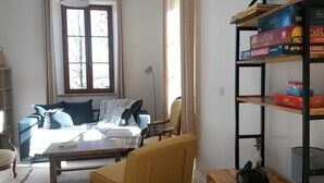 Una sala de estar con un sofá, un sillón amarillo, una mesa de centro y una estantería llena de juegos de mesa.