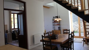 Un comedor con una mesa de madera, sillas y una lámpara colgante. Se ve una escalera al fondo.