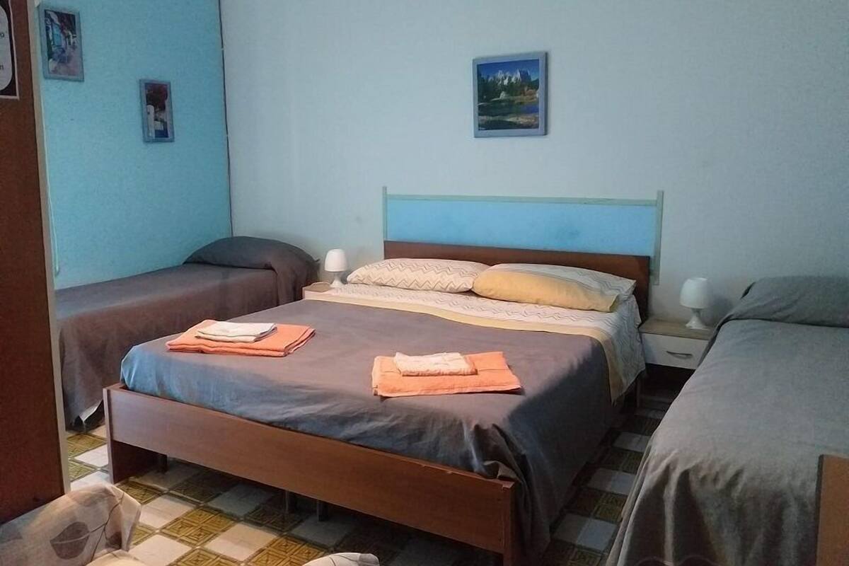 A room with two single beds, a wooden headboard, a small bedside table with a lamp, and a wall-mounted picture.