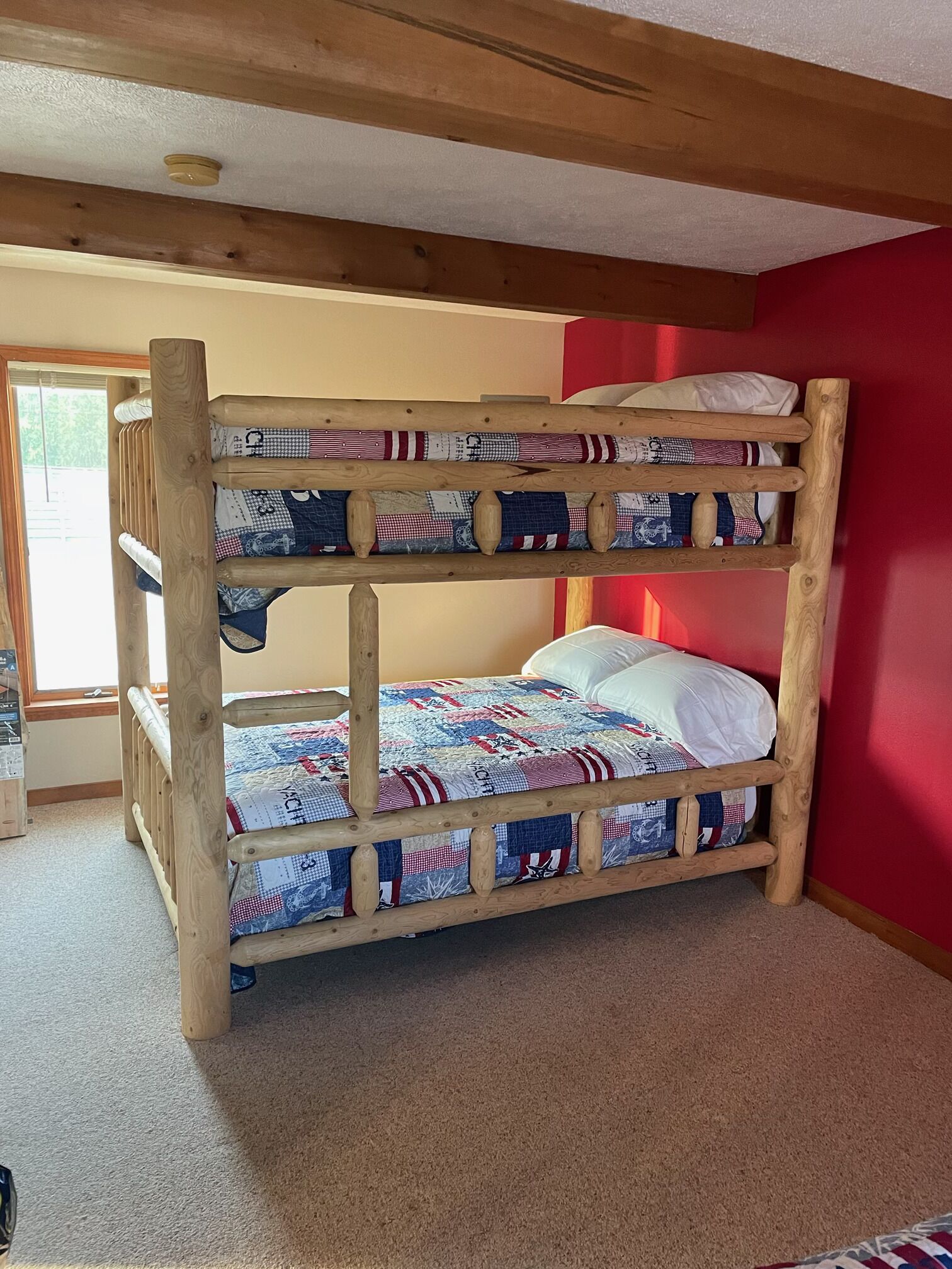 Una cama litera con colcha acolchada, estructura de madera y pared roja.