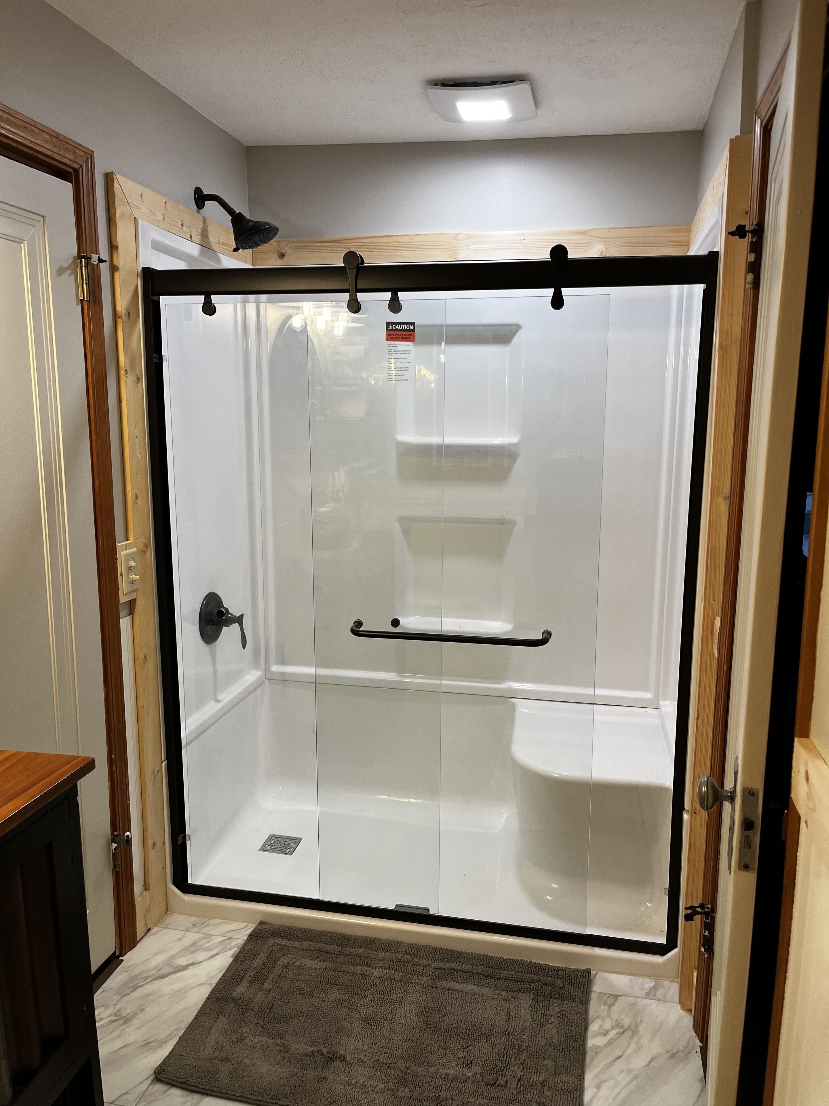 Une douche à l’italienne avec une porte en verre, un cadre en bois et une poignée en métal.