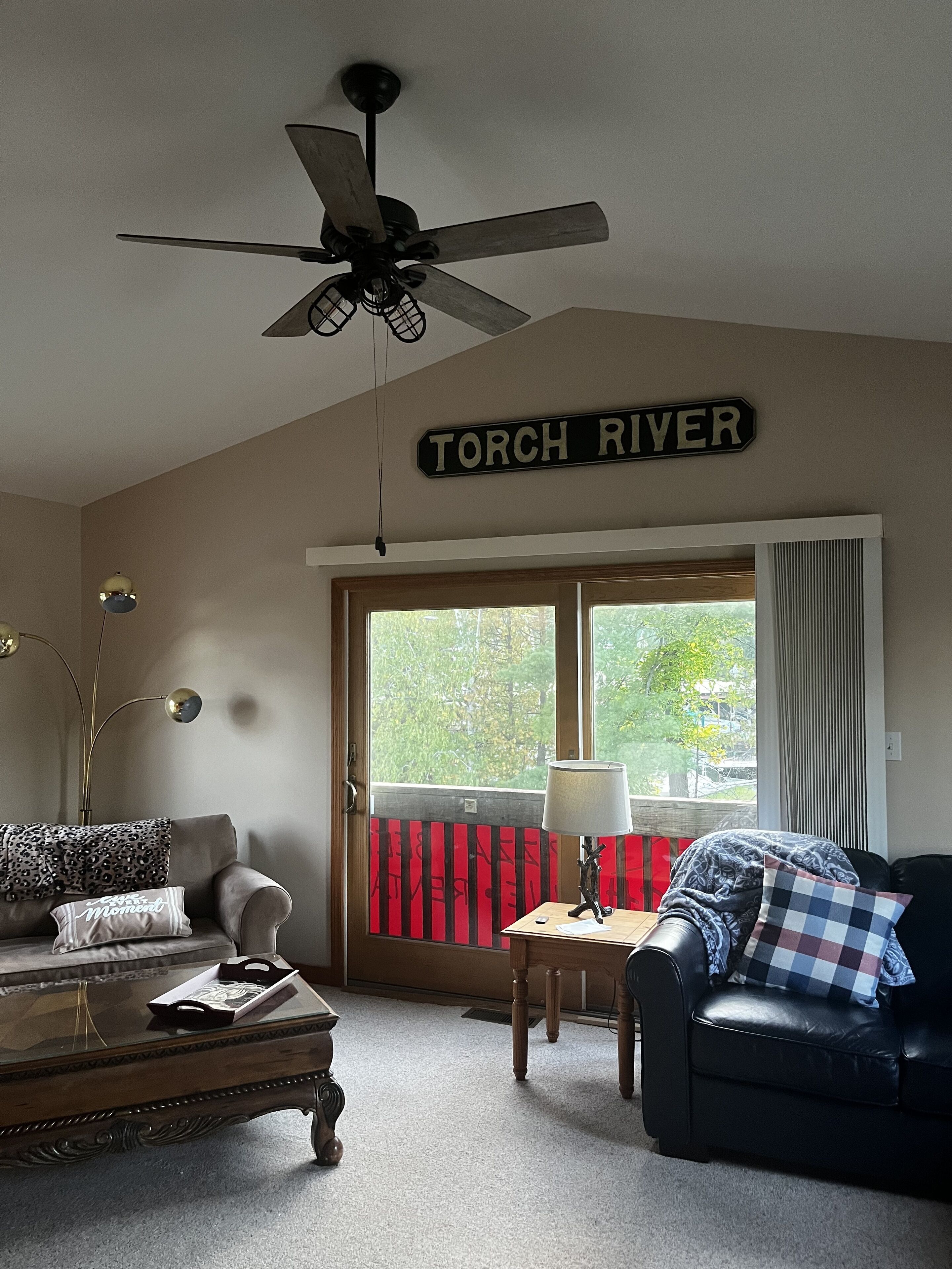 Un salon doté d’un ventilateur de plafond, d’une enseigne indiquant « TORCH RIVER », d’un canapé, d’une table basse et d’une fenêtre donnant sur des arbres.