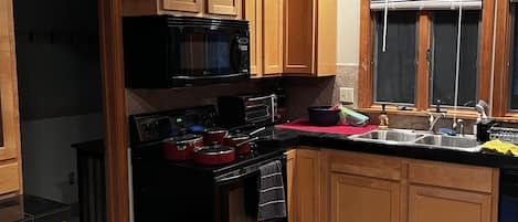 Una cocina con armarios de madera, una estufa negra, un microondas y una ventana con persianas.