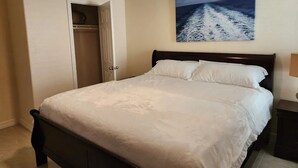 A bedroom with a bed, a ceiling fan, a painting of a seascape, and a door leading to a closet. - Cozy Glen Abbey retreat-sleeps-6 (Houston)