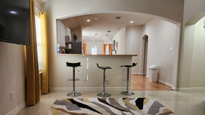 A modern kitchen with a central island, three bar stools, and a patterned rug. - Cozy Glen Abbey retreat-sleeps-6 (Houston)