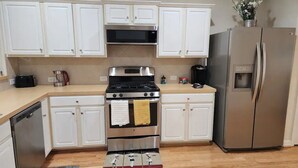 A kitchen with white cabinets, a stainless steel stove, a refrigerator, and a wooden floor. - Cozy Glen Abbey retreat-sleeps-6 (Houston)