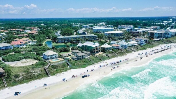 An aerial view of a coastal resort with multiple beachfront villas, a sandy beach, and a clear view of the ocean.