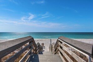 A wooden boardwalk leading to a beach with clear blue water and a sandy shore.