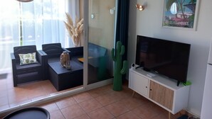 A modern living room with a sofa set, a television, a cactus, and a sliding glass door leading to an outdoor area. - Studio Proche Mer, son Jardinet et sa Place de Parking Privés (Roquebrune-sur-Argens)