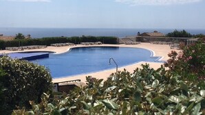 A swimming pool with a curved edge, surrounded by lounge chairs and a view of the sea. - Studio Proche Mer, son Jardinet et sa Place de Parking Privés (Roquebrune-sur-Argens)