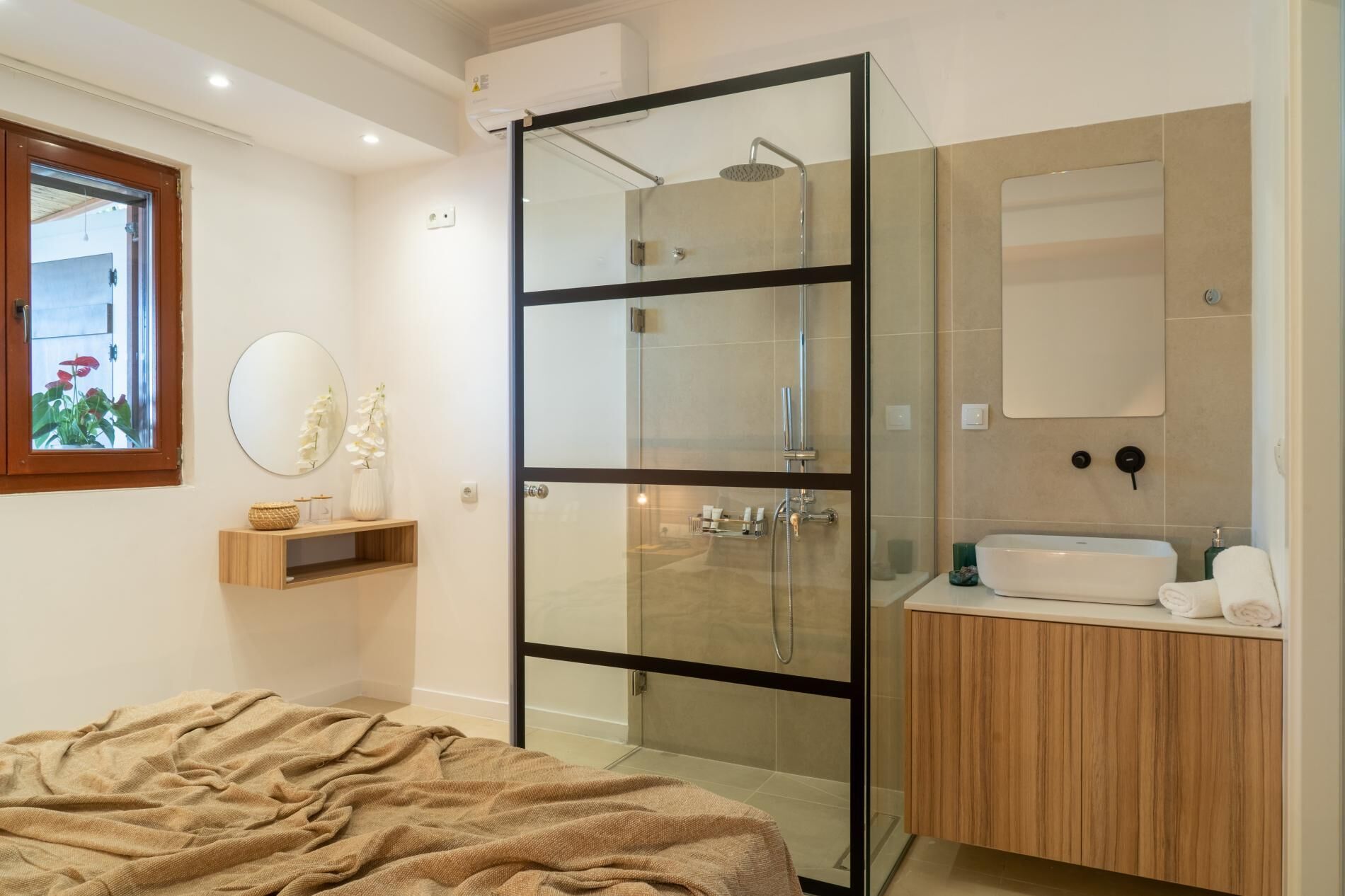 Een moderne badkamer met een douchecabine van glas, een houten wastafelmeubel en een ronde spiegel.