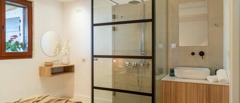 Een moderne badkamer met een douchecabine van glas, een houten wastafelmeubel en een ronde spiegel.