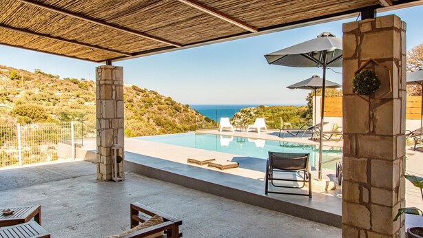 A pool area with a view of the sea, stone pillars, and outdoor seating. - Canyon 2 villa with private pool (Rethymno)