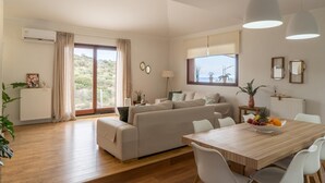 A spacious living area with a sofa, dining table, and large windows offering a view of the outdoors. - Canyon 2 villa with private pool (Rethymno)