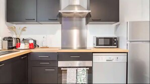 A modern kitchen with dark cabinets, a stainless steel range hood, a microwave, and a dishwasher.