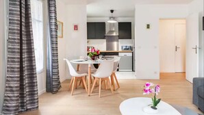 A modern living room with a dining area, a kitchen, and a door leading to another room.