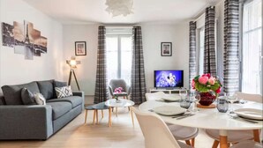 A modern living room with a grey sofa, a small round table, and a dining area with a white table set for four.