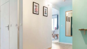 A hallway with white walls, two framed pictures, a wooden floor, and a door on the left.