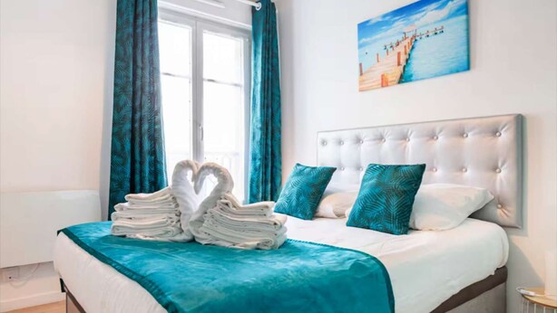 A neatly made bed with a teal bedspread, two teal pillows, and a white headboard.