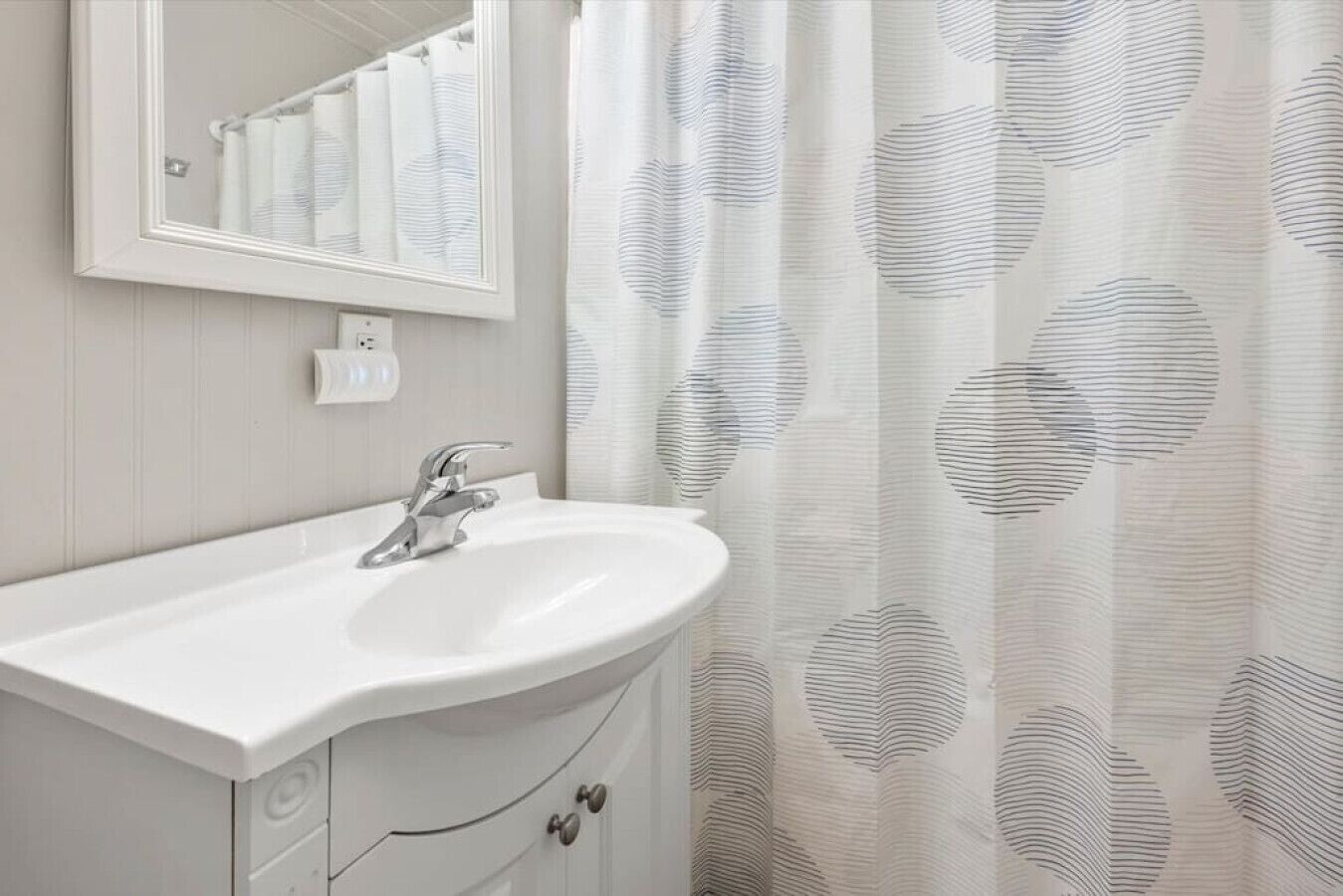 Un bagno con un lavandino bianco, uno specchio e una tenda da doccia con motivo circolare.