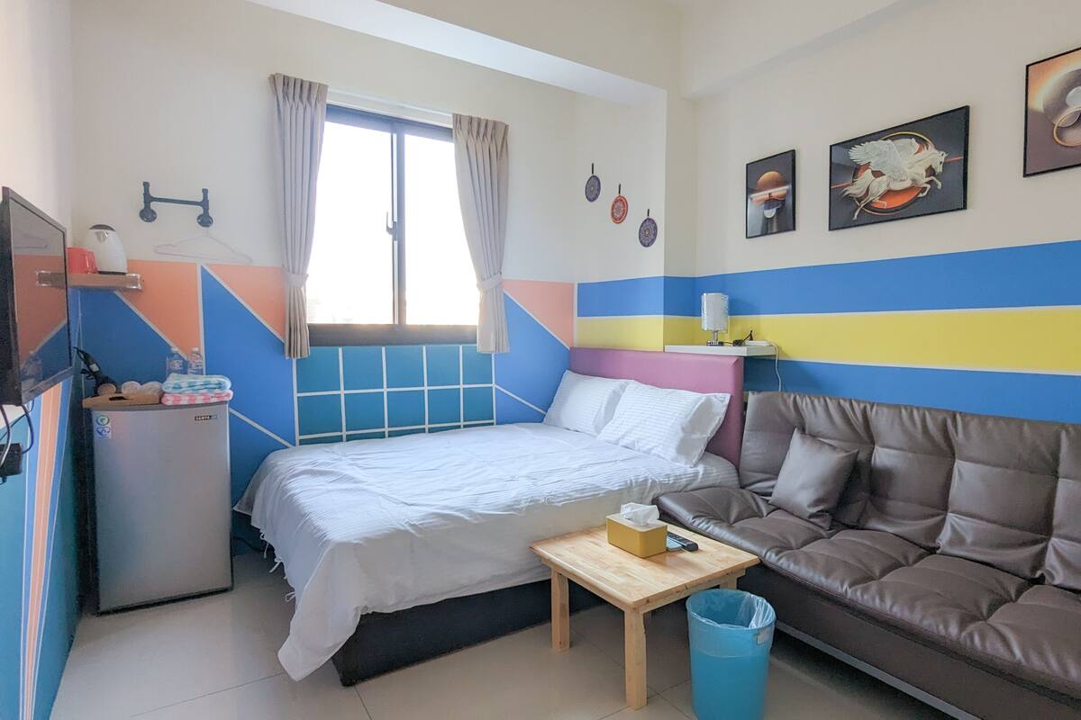 A compact room with a bed, a sofa, a small table, and a TV.
