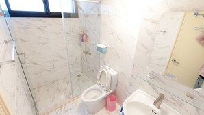 Ein Badezimmer mit Duschkabine aus Glas, Toilette, Waschbecken und Spiegel.
