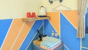 Ein Zimmer mit einem Bett, einem kleinen Tisch mit Wasserkocher, Tassen und Wasserflaschen.
