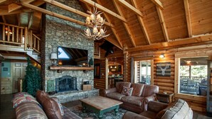 A log cabin interior with a stone fireplace, leather furniture, and a mounted deer head.