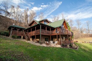 Situated in a wooded area, this cabin features a wrap-around deck and a steeply pitched roof.