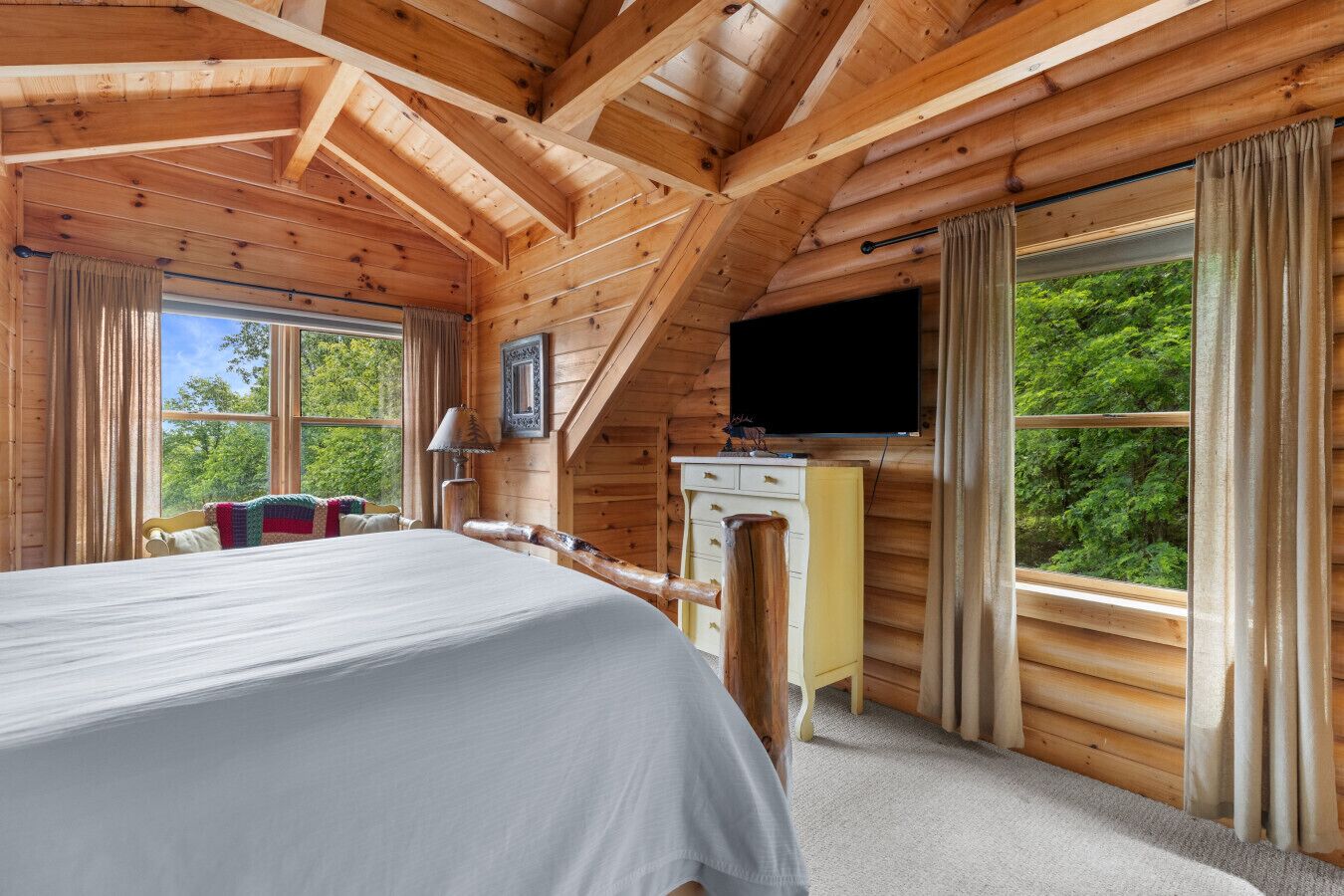 A log cabin bedroom with a bed, a desk, and a TV.