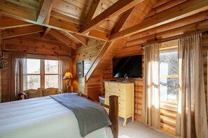 Cozy bedroom with a large bed, wooden dresser, and TV, offering a view of the outside through two windows.