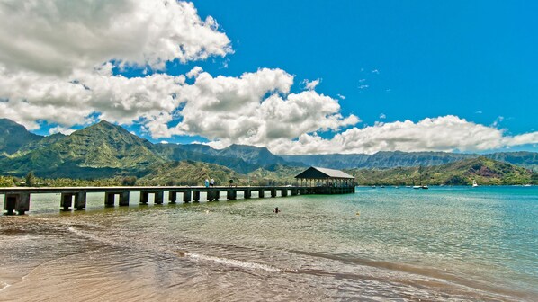A pier extending into a clear blue sea with mountains in the background.