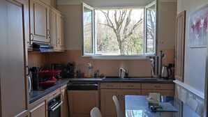 A kitchen with wooden cabinets, a dining table with chairs, a window with a view of trees, and a ceiling light fixture.