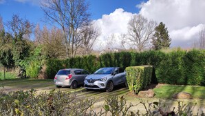 A parking area with two cars parked next to a hedge.