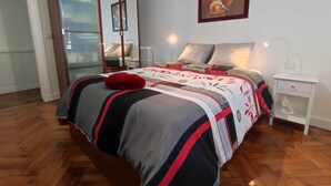 A bedroom with a bed, a nightstand, a lamp, a red pillow, and a painting on the wall.