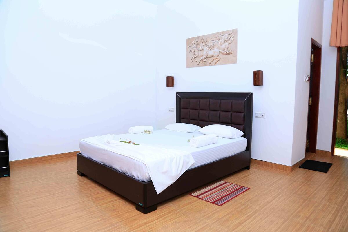 A neatly made bed with white linens and pillows, a dark headboard, and a wall-mounted artwork above it.