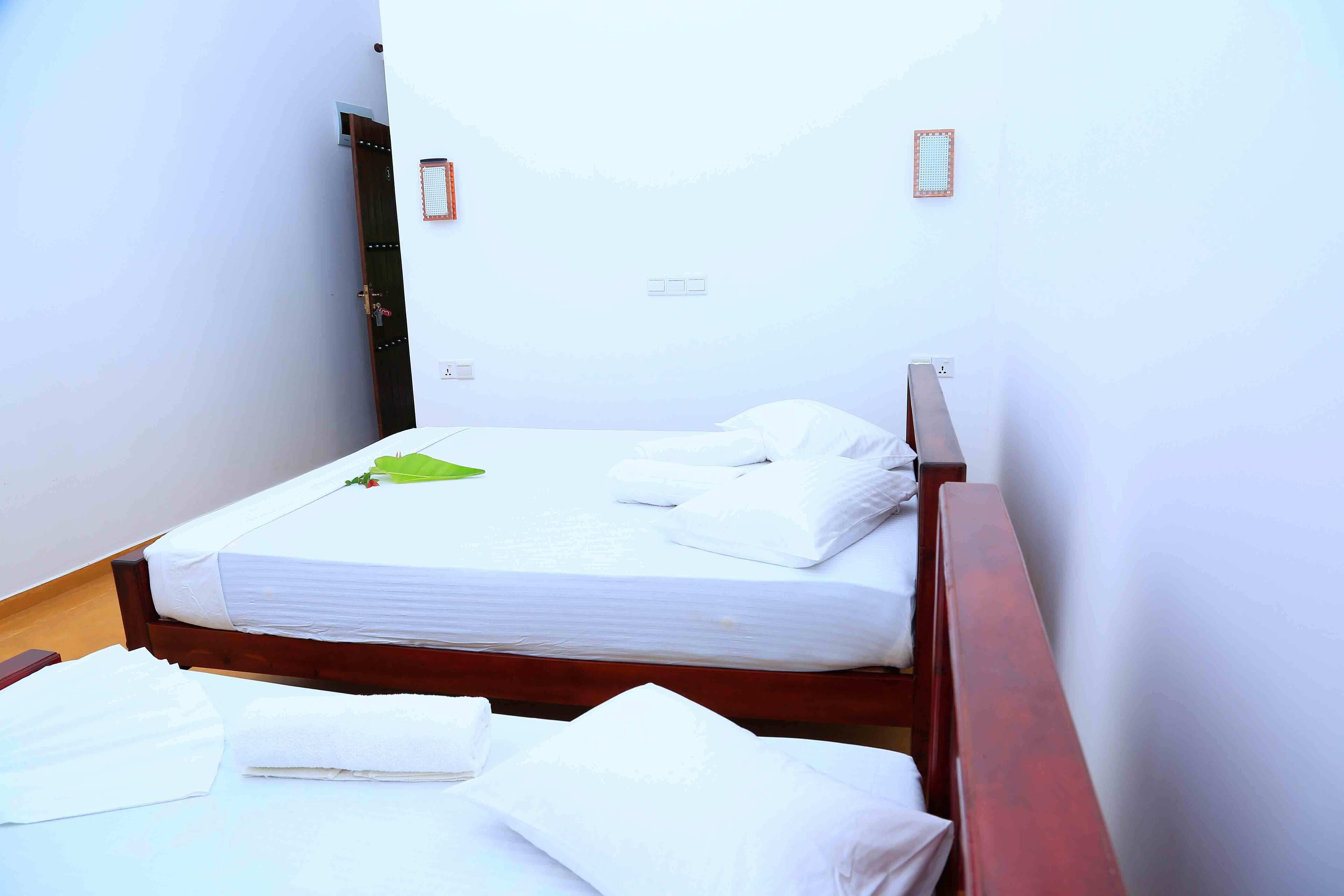 Une petite chambre avec un lit simple, un cadre en bois, du linge de lit blanc et une décoration représentant une feuille verte.