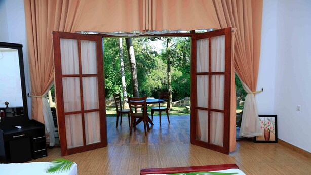 Una habitación con una cama, un escritorio y una mesa con sillas. Se ve un jardín a través de una puerta abierta.